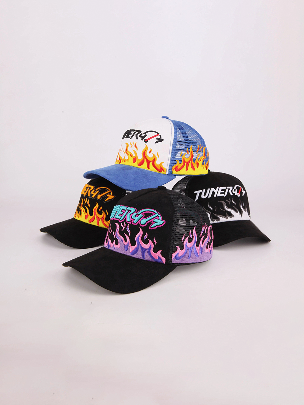 Four TUNER4/7 trucker hats with embroidered flame designs in blue and white, black and orange, black and purple, and black and white.